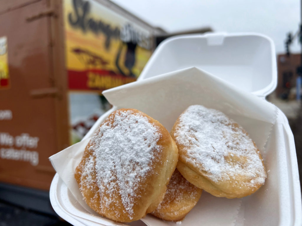 Three beignets in a white styrofoam container outside Stango Bites food truck in Champaign, Illinois.