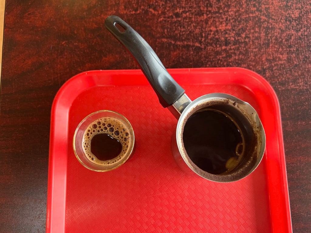 A small cup of Turkish coffee beside a small pot of coffee on a red tray.
