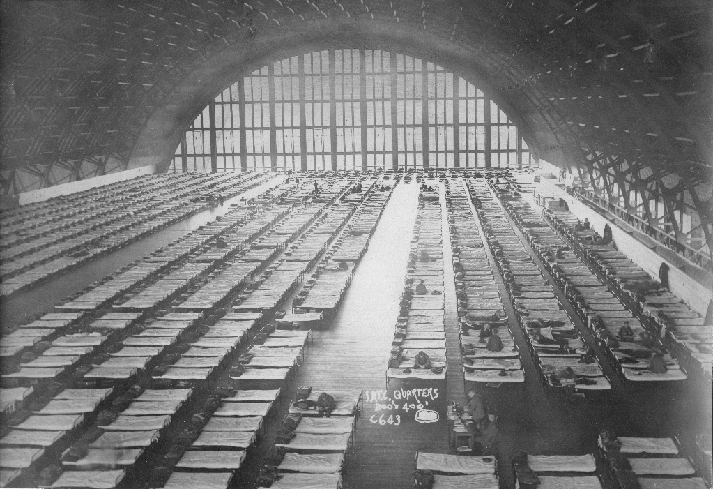 An old black and white picture of armory during World War I. The whole armory is full of cots with soldiers on some of them. 
