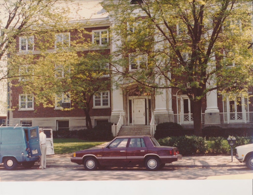 A 1984 color photo of the Busey Evans residence halls the trees have just started budding and there is an old brown car parked in the street.