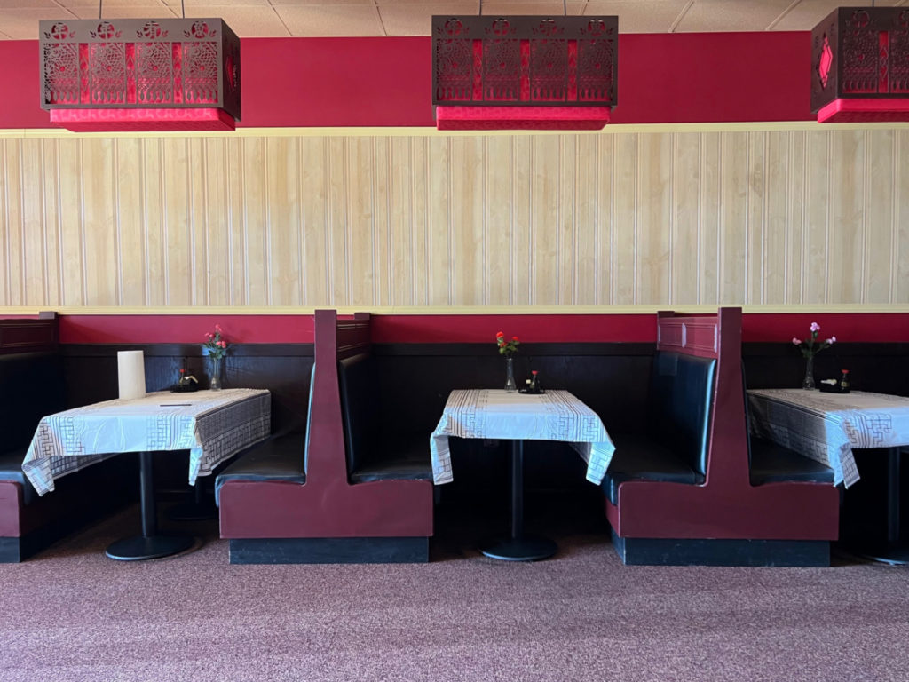 Three booths are set with a white tablecloth, a vase of flowers, and soy sauce.