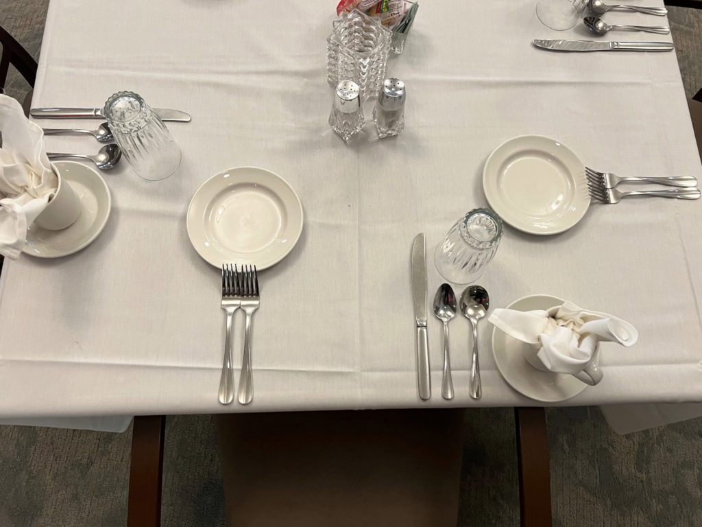 A dining table with a white tablecloth and three place settings.