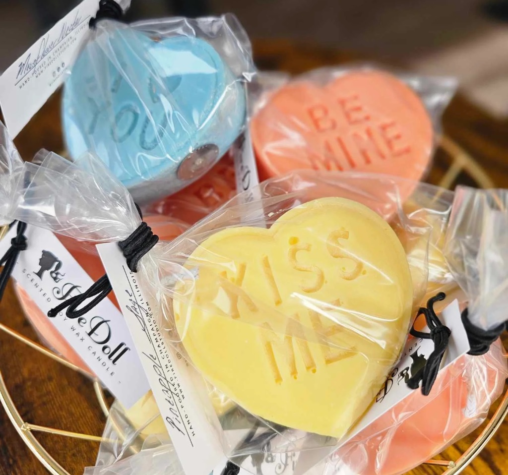 A basket of heart shaped candles in yellow, pink, and light blue. The yellow candle says "kiss me". 