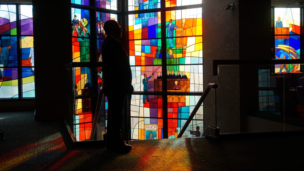 The dark outline of Henry Louis Gates Jr. is illuminated as he stands in front of huge panels of stained glass at Trinity United Church of Christ in Chicago.