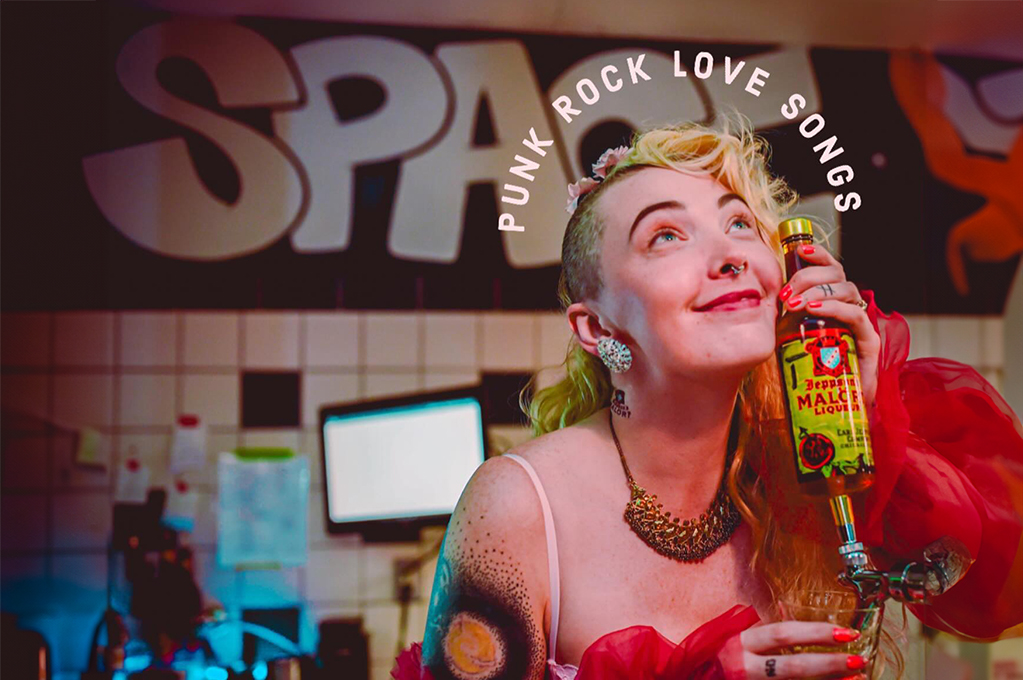 The scene is set at a bar or cafe. A person with a tattoo on their shoulder is in the foreground, holding a bottle labeled “Malort”. They are dressed in a red outfit with puffy sleeves and a necklace. The background features a wall with tiles and the text “PUNK ROCK LOVE SONGS” written on it. The atmosphere seems lively and colorful. The word "SPACE" is painted on the wall behind them.