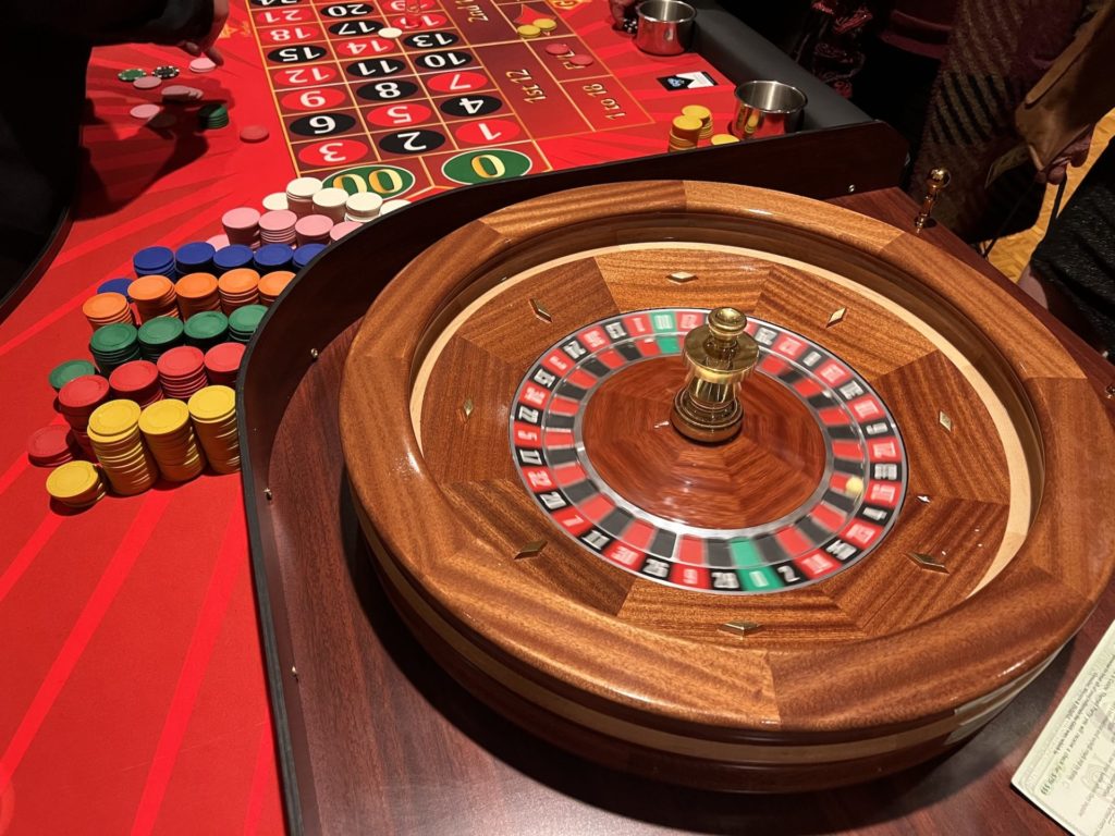 A roulette wheel on a red roulette table with different colored poker chips.