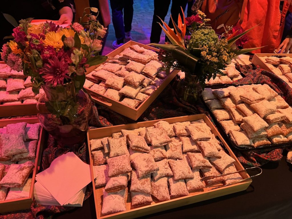 Trays of beignets on a table decorated with flowers in vases and different fabrics.