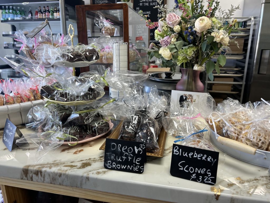 Various individually wrapped baked goods and treats on the counter with a large bouquet of flowers sitting behind.