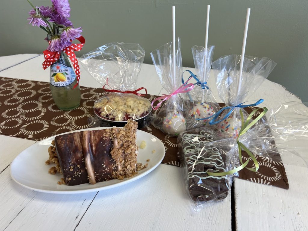A large slice of cake sits next to cake pops, a chocolate mint brownie, and mini tart. 