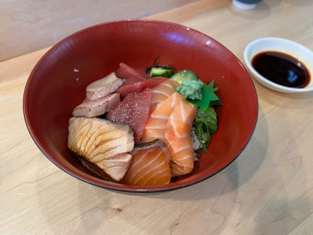 A bowl of kaisen don (tuna and salmon) over steamed rice with a side bowl of soy sauce.