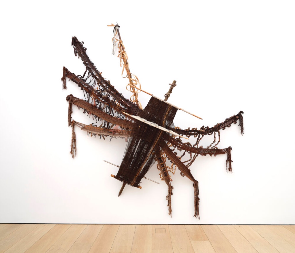 A multimedia textile where the artist has handwoven brown threads into the shape of a large spider. The artist has incorporated elements of the loom to add to the body and structure of the spider
