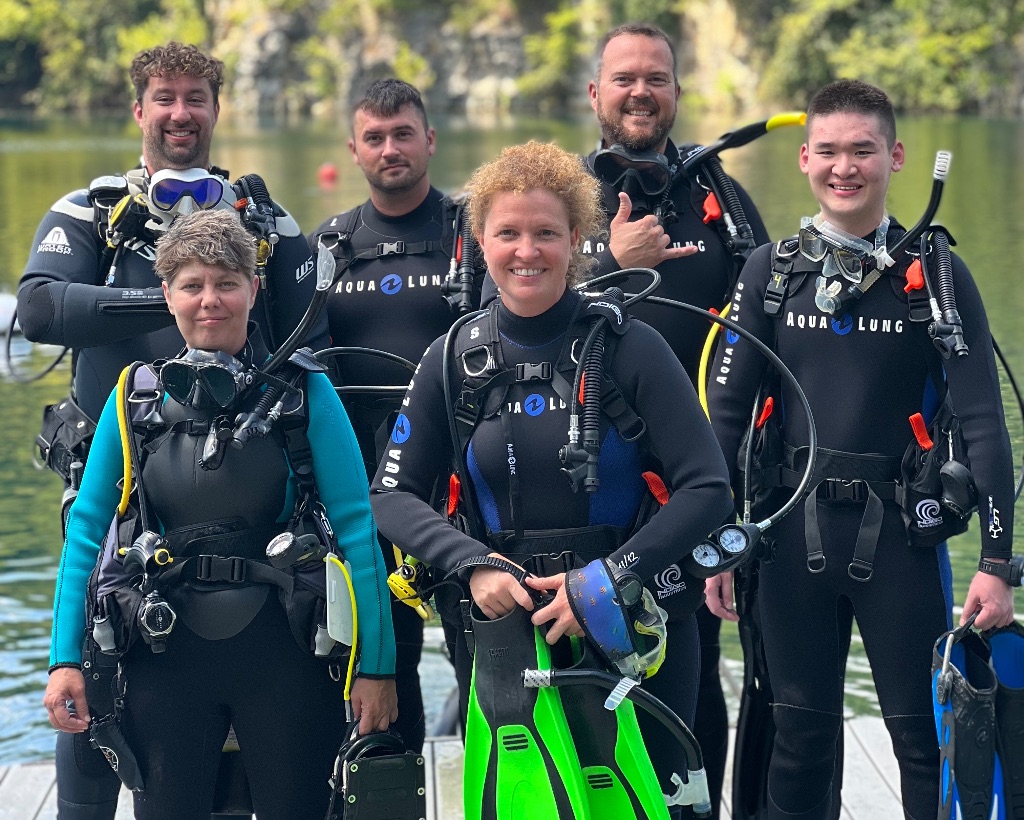 A group of six people stand in full scuba gear for the final stage of open water certification in Mermet Springs in Southern Illinois, Gentner is top-left.