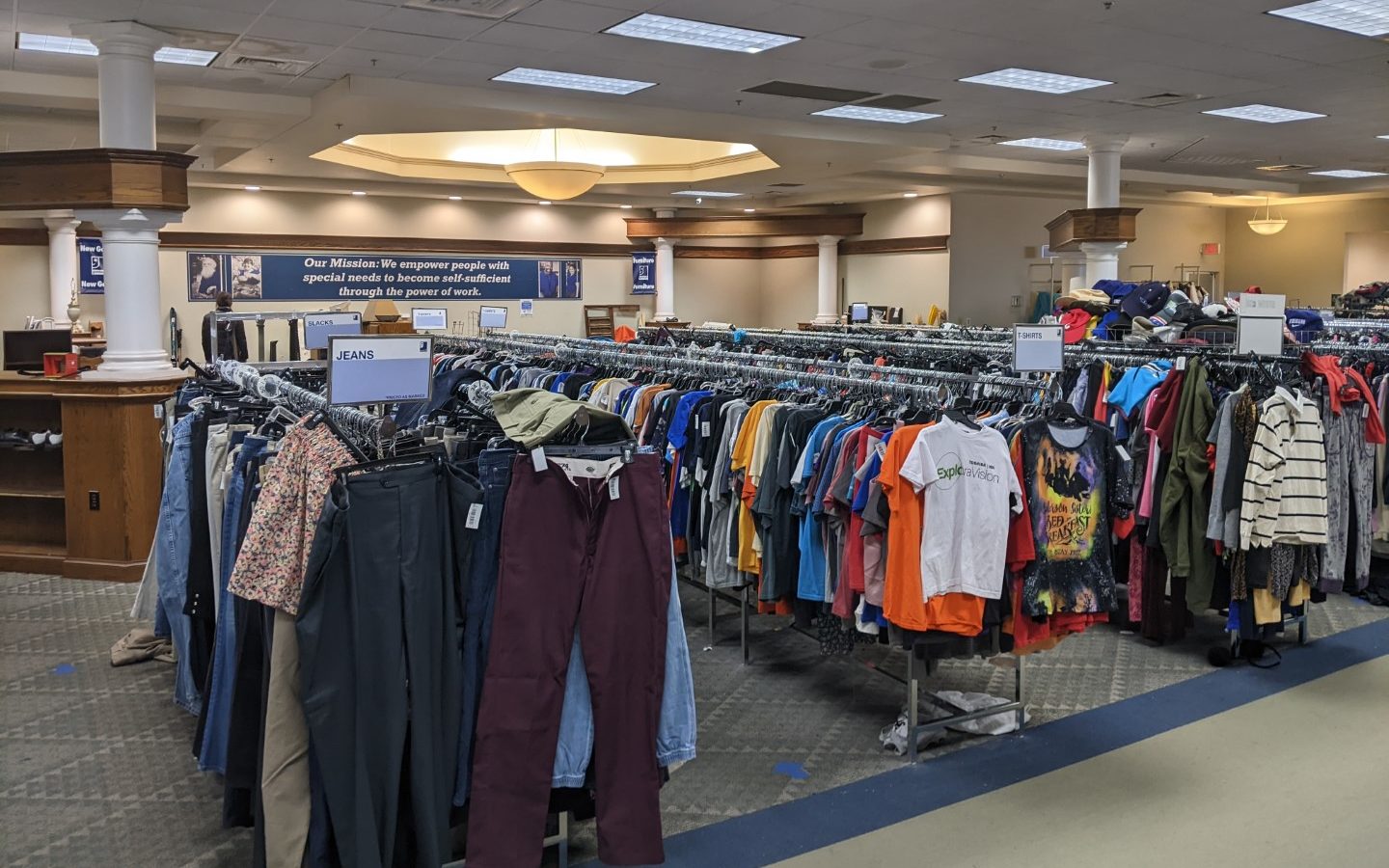 The inside of the goodwill store. Long racks of clothes are visible. And white columns are against the walls. 