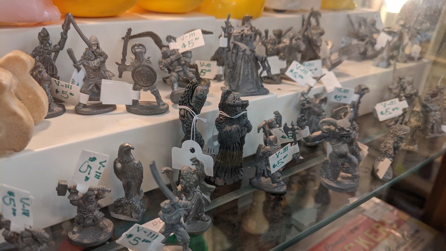 A shelf of many pewter figurines, people, animals, and other objects displayed on a glass shelf. 