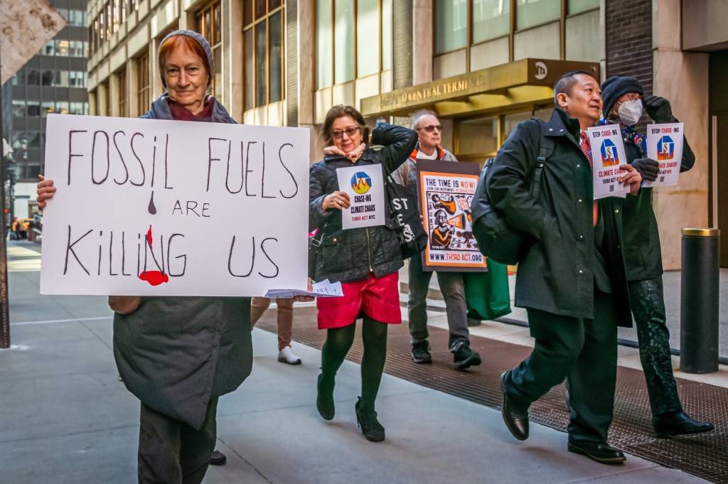 A group of people are walking down a street holding protest signs about fossil fuels. 