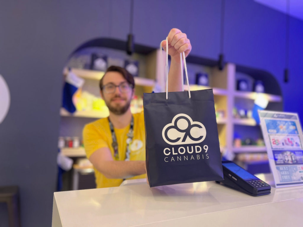 A staff person is handing a bag with Cloud9 Cannabis on it to the customer.