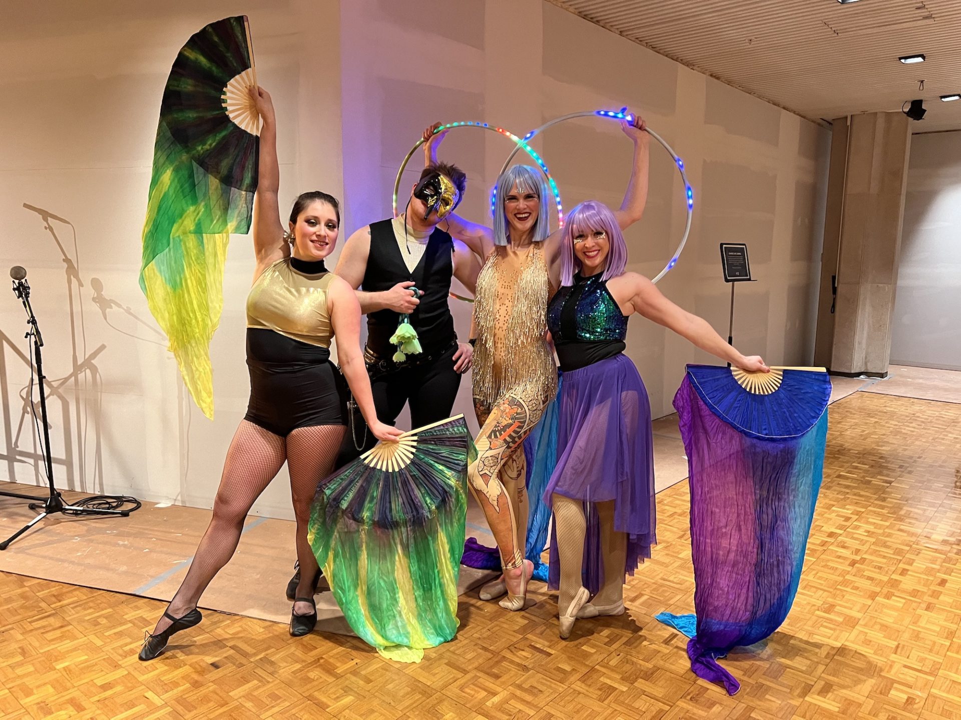 Four performers from Carnaval. Three woman and one man in acrobatics outfits. Two women have fans with fabric and one woman hold two hula hoops above her head.