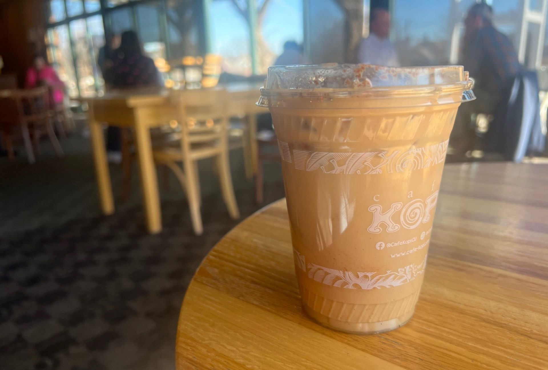 An iced latte in a clear plastic cup, sitting on a round wooden table in Espresso Royale.