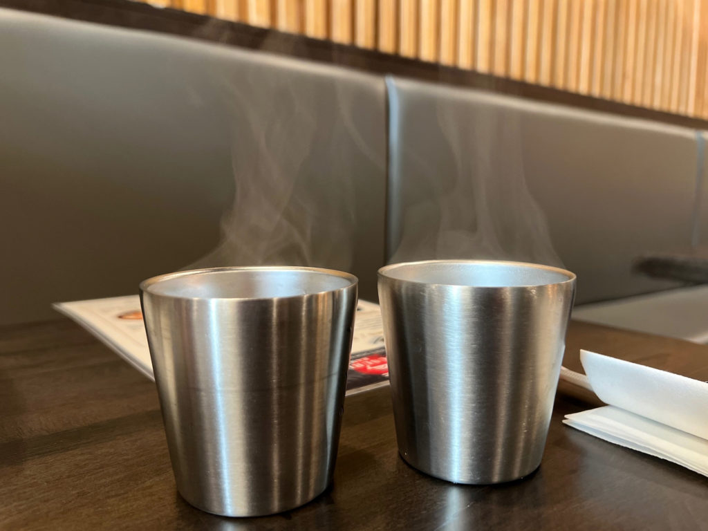 Two metal cups with very hot tea and steam rising from the cups.
