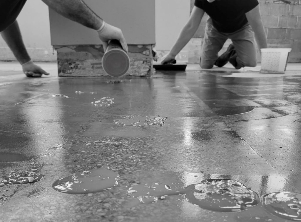 Black and white image of two people patching and smoothing flooring. 