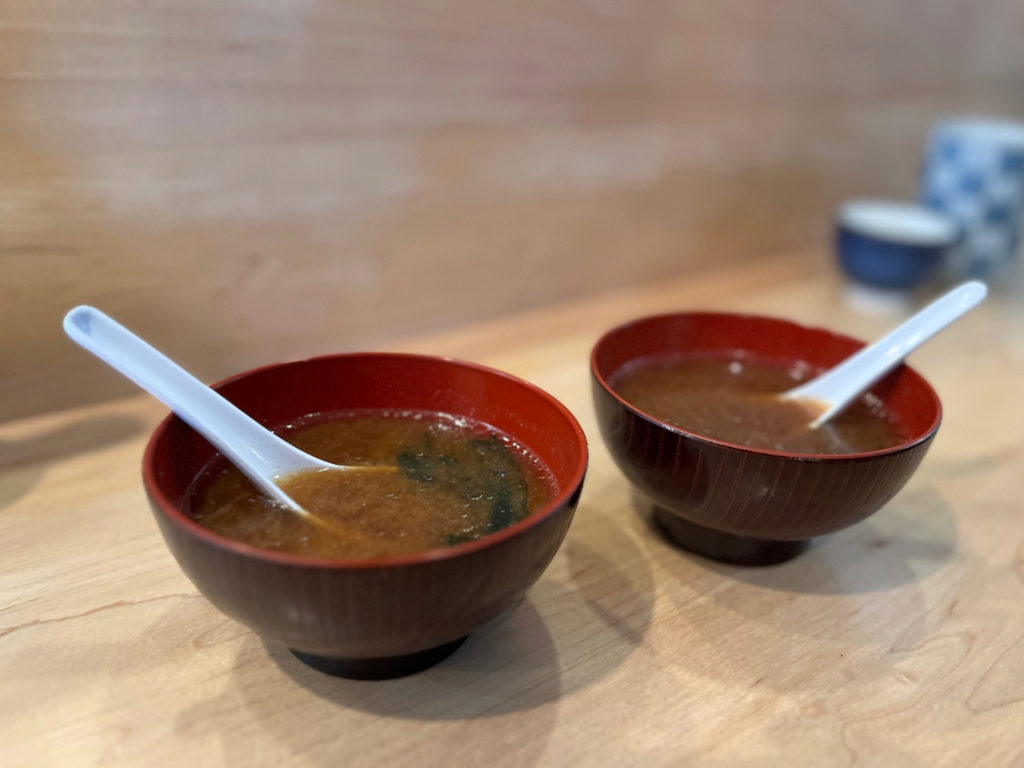 Two bowls of miso soup with white spoons.