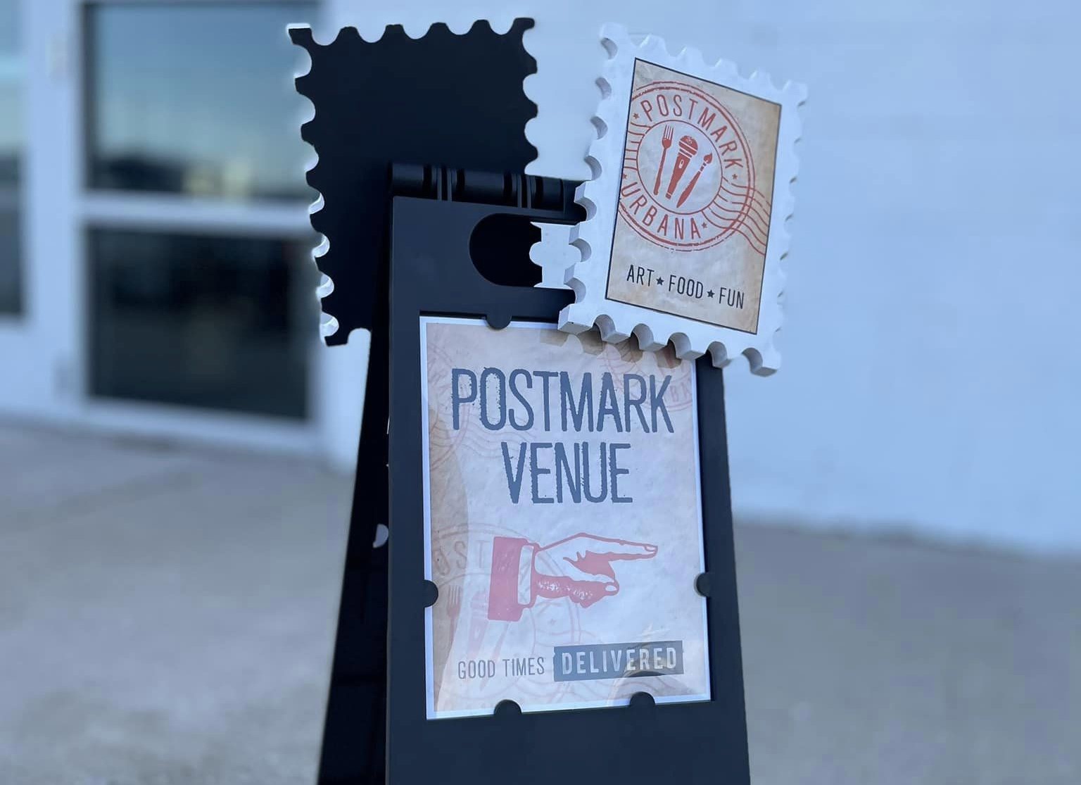 A black sandwich board with a sign that says PostMark Venue and a hand pointing to the right.