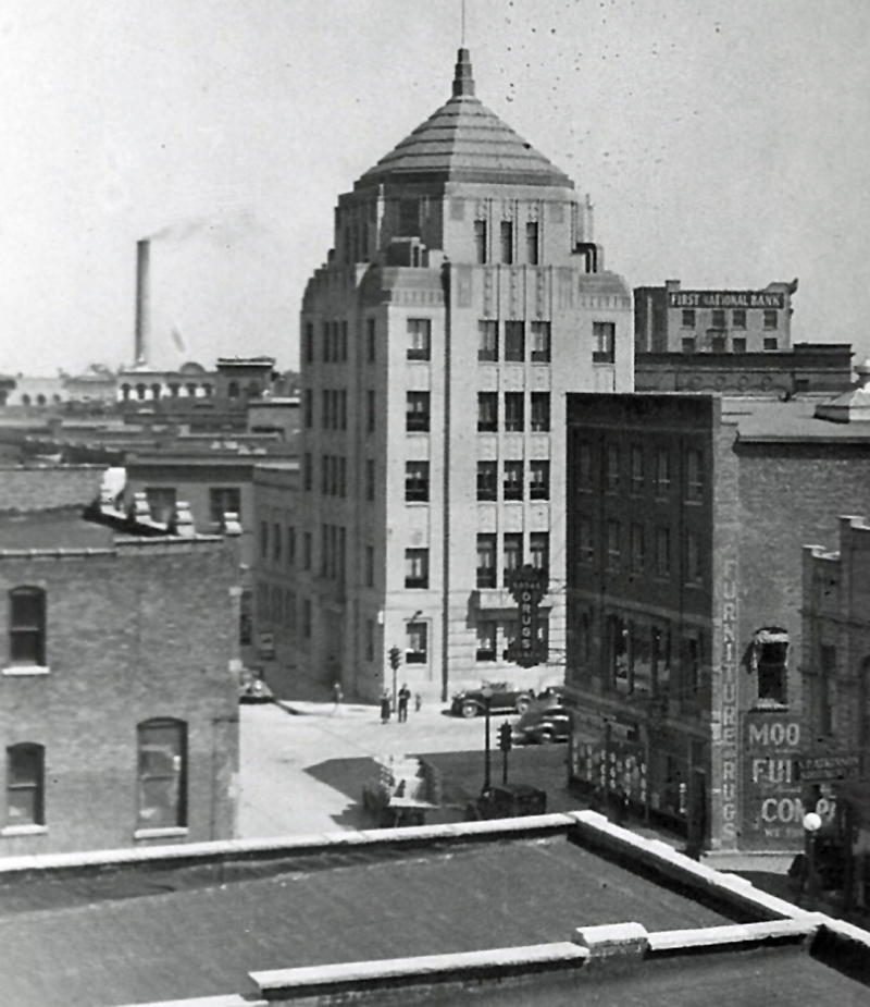 An old black and white picture of the city of champaign building. The six story building has a pointed top and is surrounded by streets with cars on them.