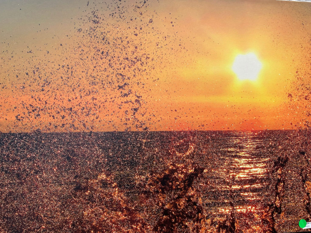 High resolution photograph of a bright orange sunrise over Lake Michigan with water droplets suspended in midair.