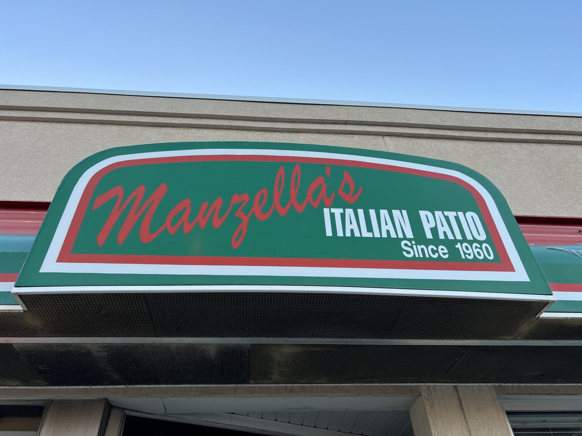 Close-up of Manzella's outdoor sign which is bright green with red and white writing