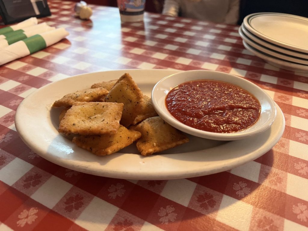 Fried ravioli sit on a plate with a small bowl of marinara