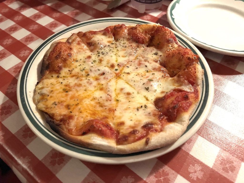 Small cheese pizza on a table with a red checked tablecloth