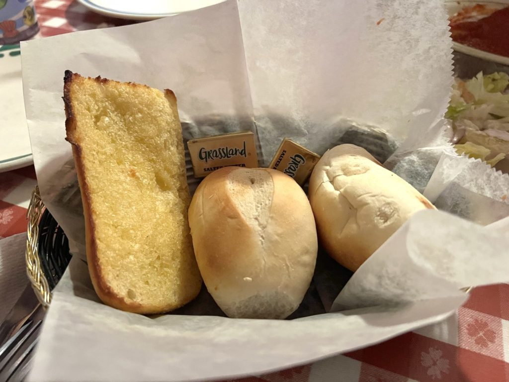 A basket of bread with garlic bread on the left and two dinner rolls.