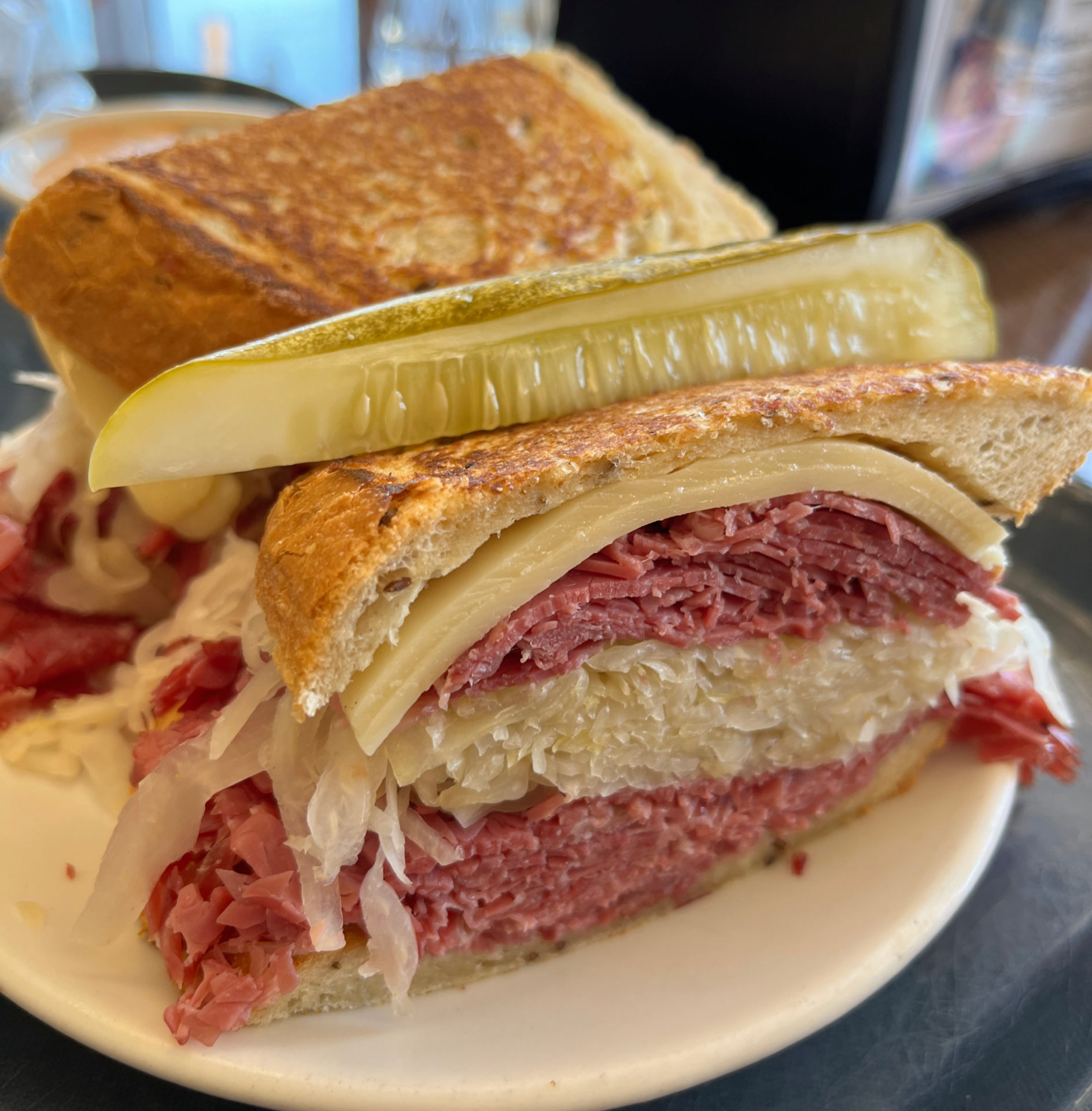 A huge Reuben sandwich with a large ribbon of sauerkraut between the corned beef. There is a pickle spear on top on one half.