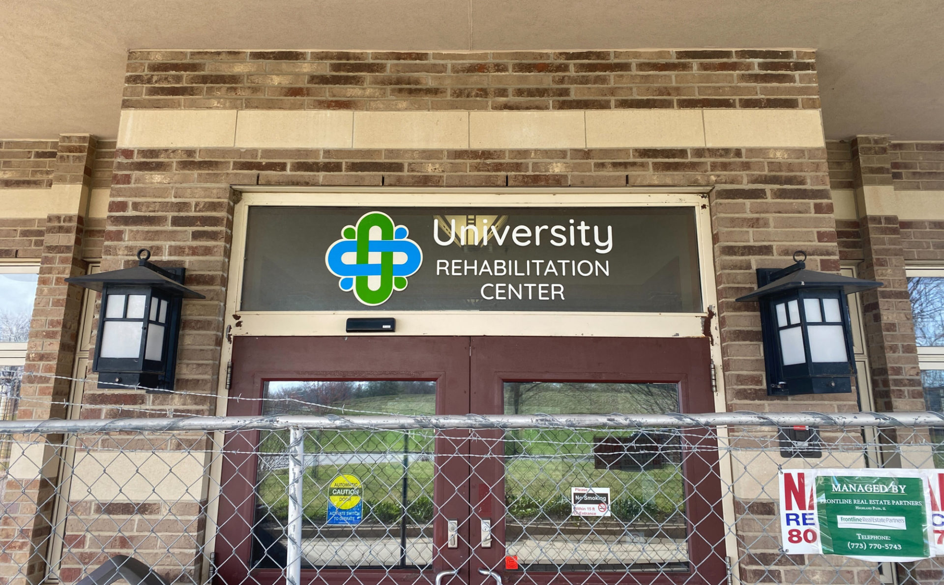 Entrance to the Champaign County Nursing Home / University Rehabilitation Center. There is a large chain link and barbed wire fence in front of the entryway, around the entire building.