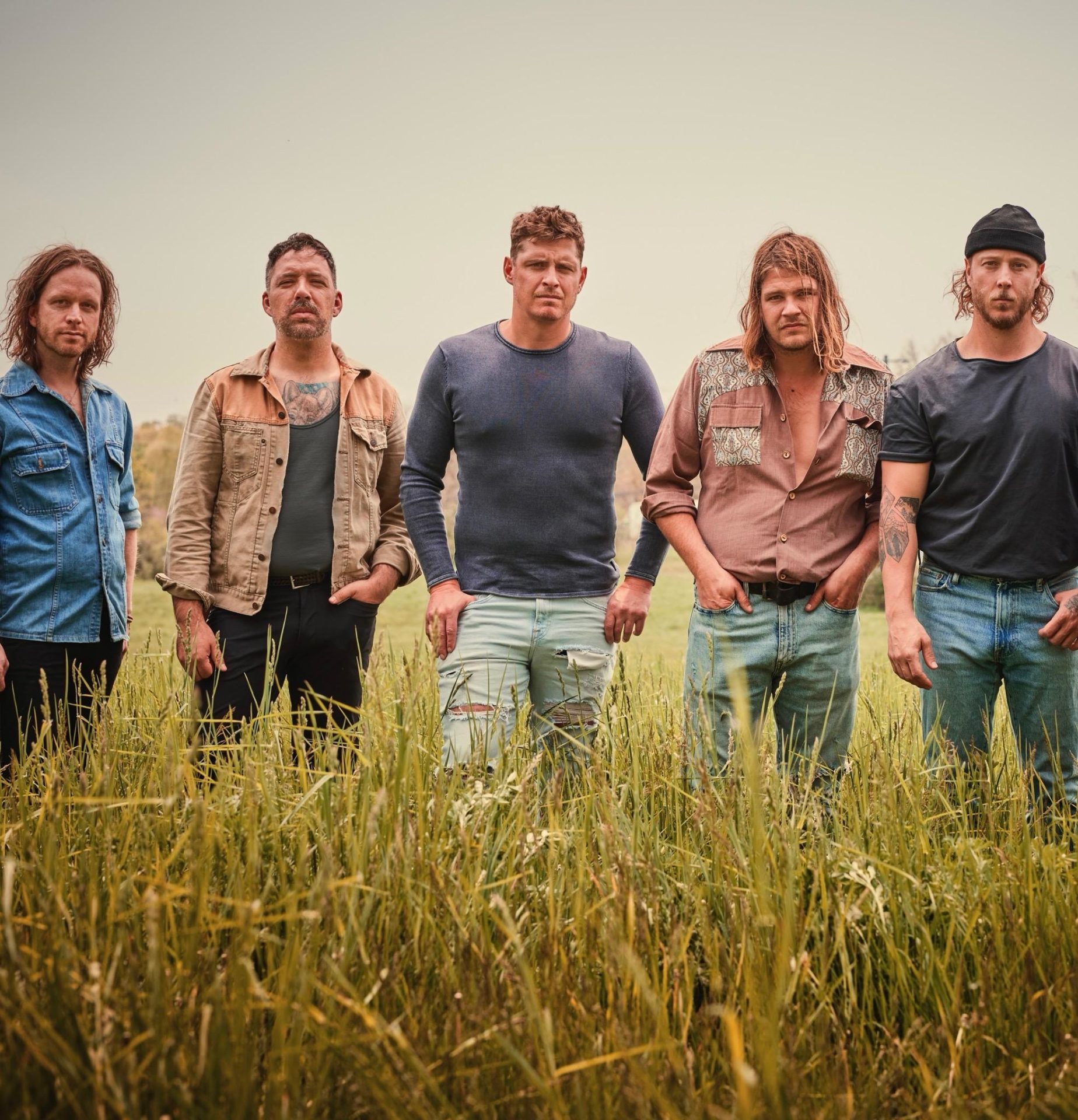 5 band members of The Glorious Sons standing in a field of grass.