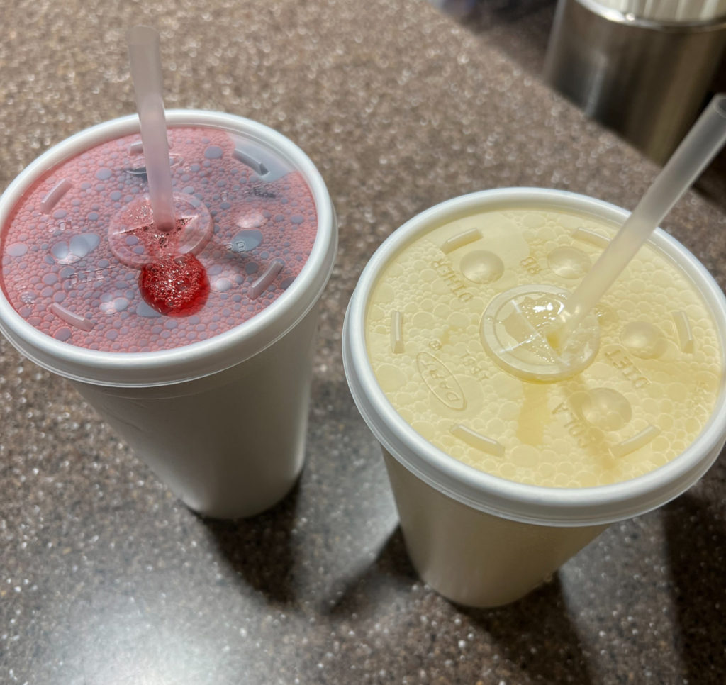 Two white styrofoam cups filled with ice and agua frescas: hibiscus and pineapple flavors.