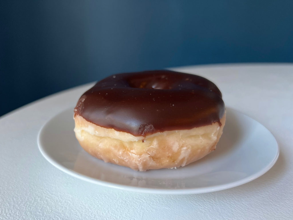 A chocolate frosted doughnut on a white plate on a white table.