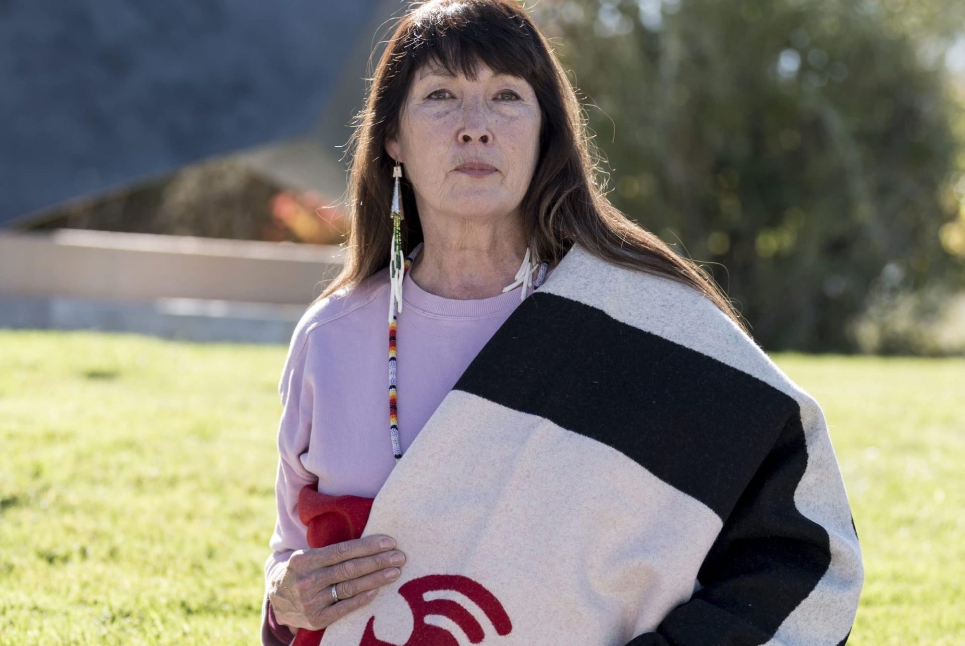 An indigenious woman with long dark hair, with a native blanket draped over one shoulder