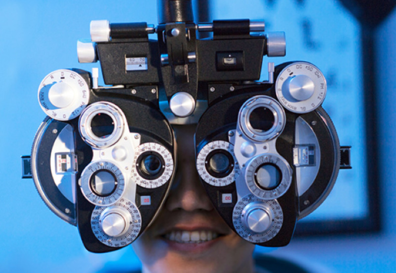 A person's face is behind a phoropter, as they receive an eye exam.