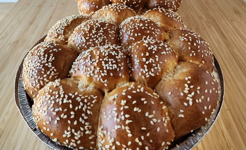 A round tray of golden brown pull apart bread with sesame seeds.