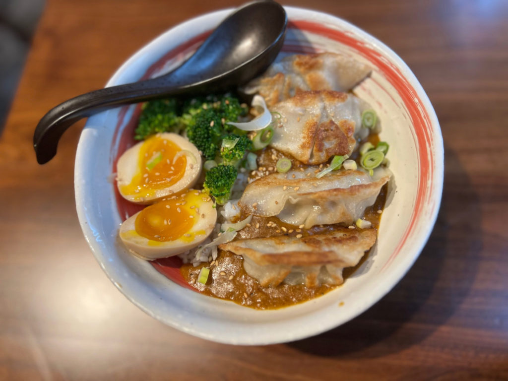 A rice bowl with gyoza, egg, broccoli, and curry sauce over white rice.