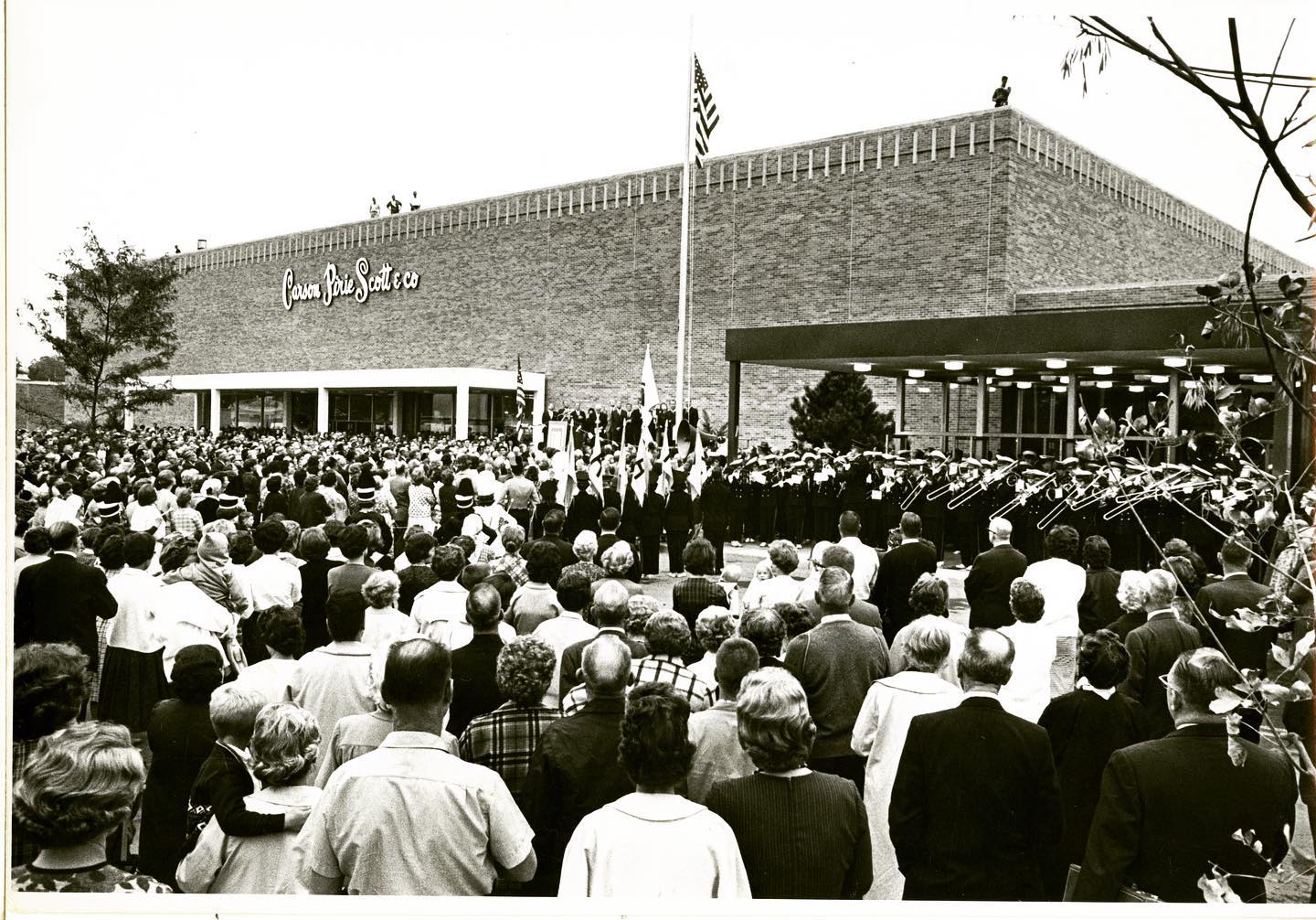 A black and white picture of the opening day of Lincoln Square Mall. Hundreds of people are gathered in front of the entrance and on the right side is a band wearing dark uniforms with white sashes. 