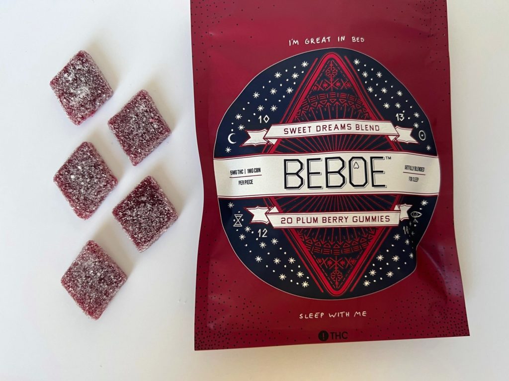 Beboe plum berry gummies shaped like diamonds, five of them arranged on a white surface in front of the reddish-purple bag.