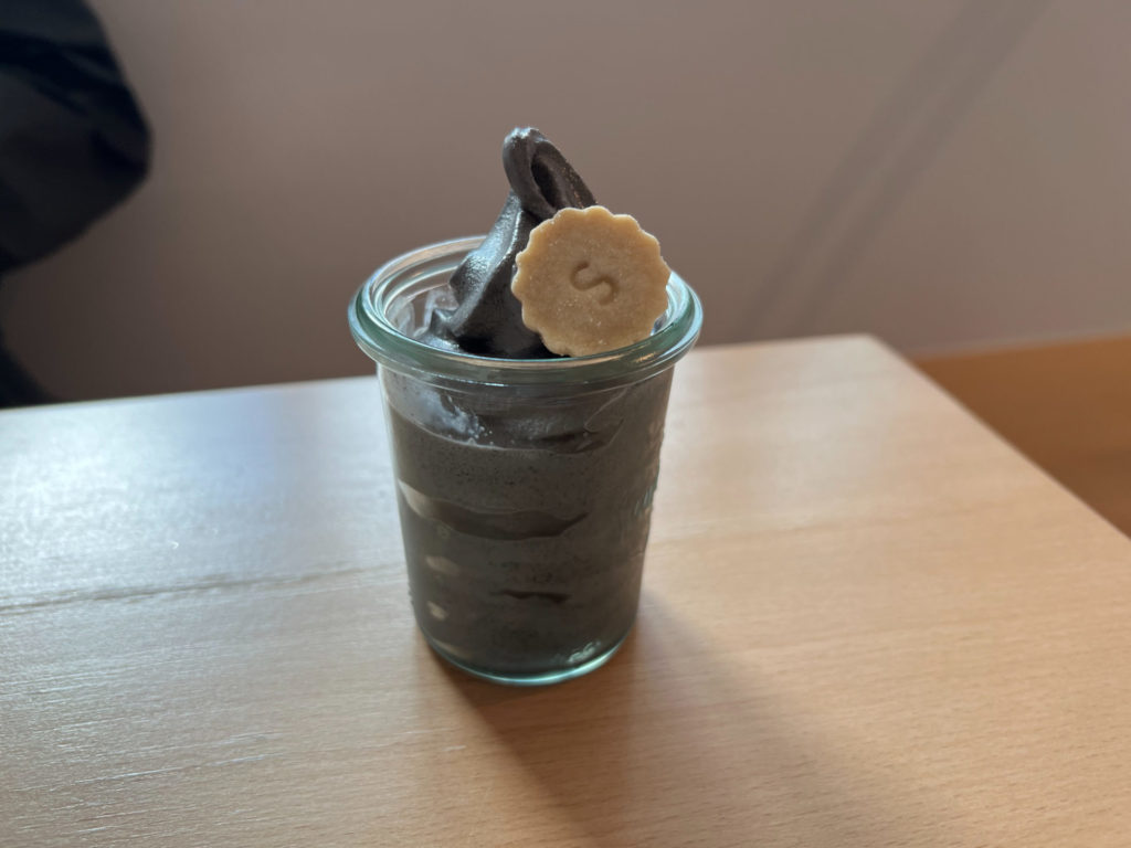 A glass cup of black soft serve with a small scalloped-edged shortbread cookie.