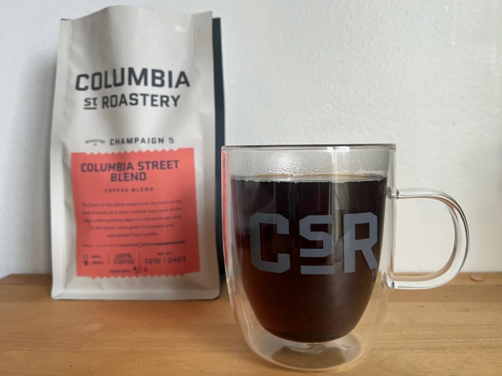 A glass mug on a wooden counter with a bag of Columbia Street Roastery Columbia Street blend on it.