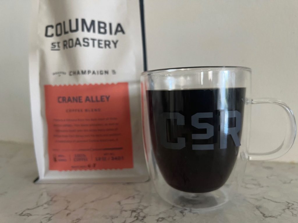 A glass mug with dark coffee and a bag of Columbia Street Roastery Crane Alley coffee in the background.