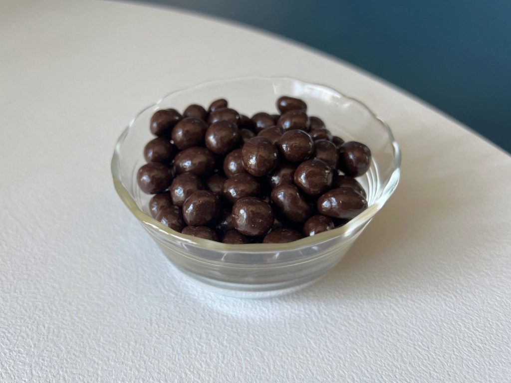 A glass bowl of espresso beans on a white table.