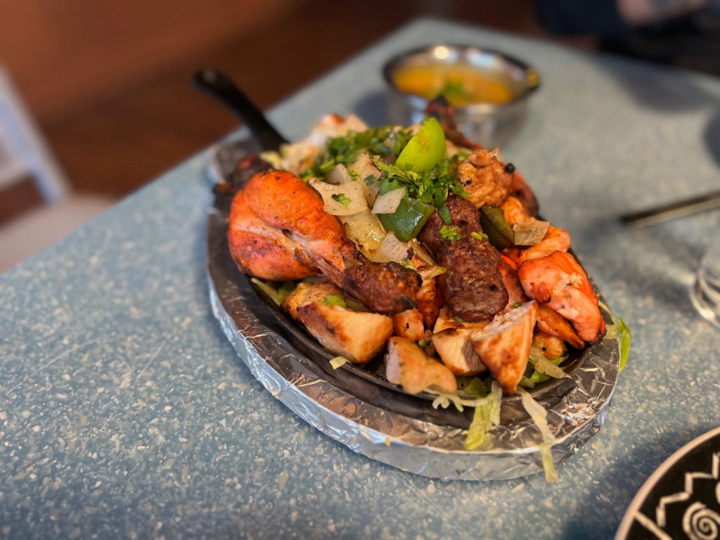 On a black cast iron skillet, it's a grilled plate of meat at Masala Indian House.