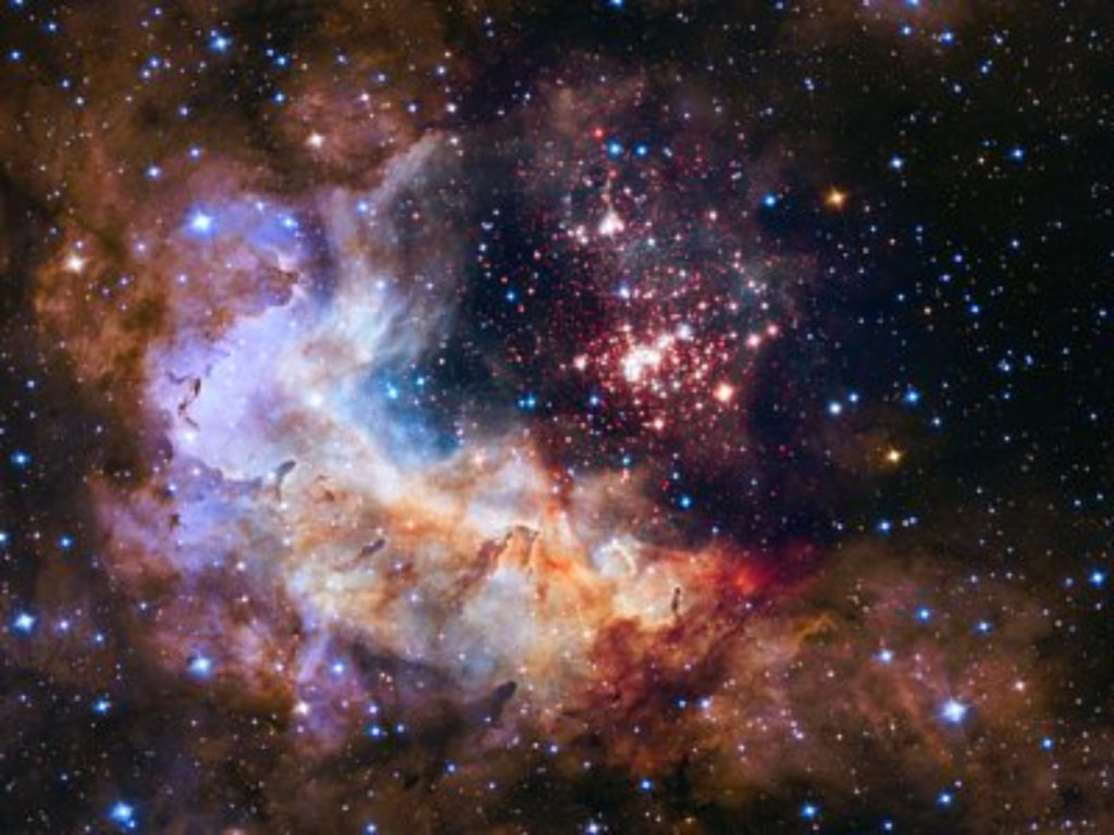 Photo image of galaxies with a dark black sky. Bursting forth is white and red and blue clouds of stardust and hundreds of points of blue and white light.