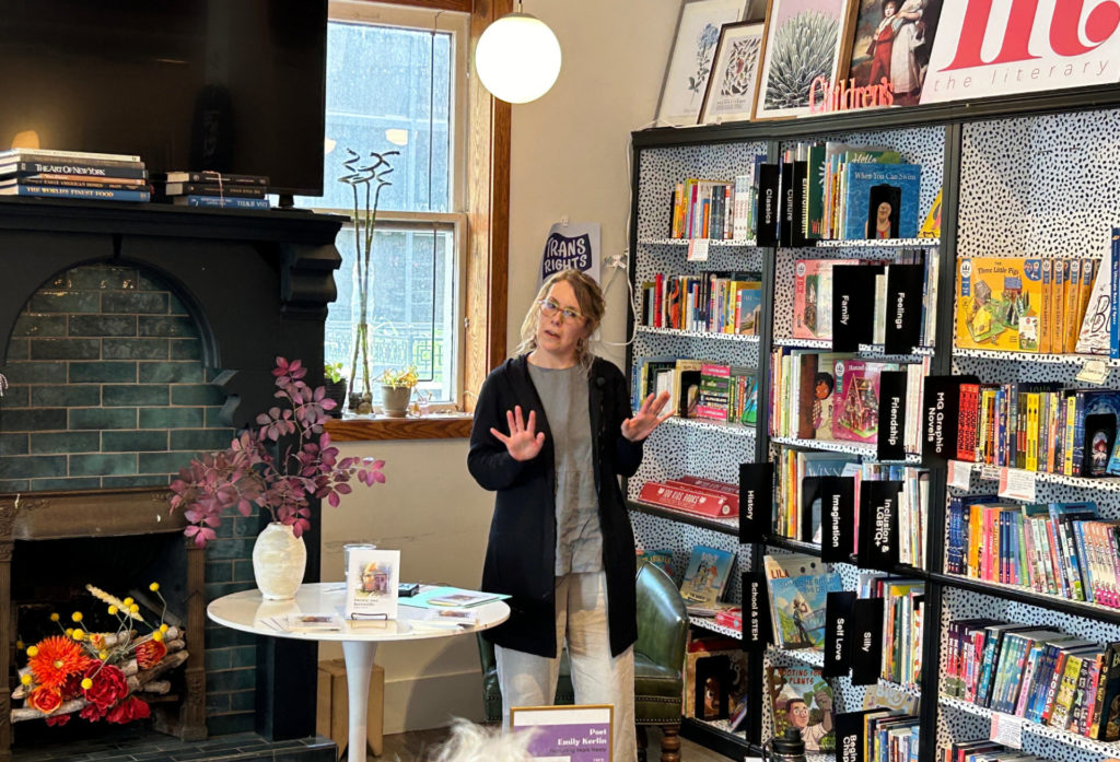 A white woman in a black sweater stands in front of shelves of books.